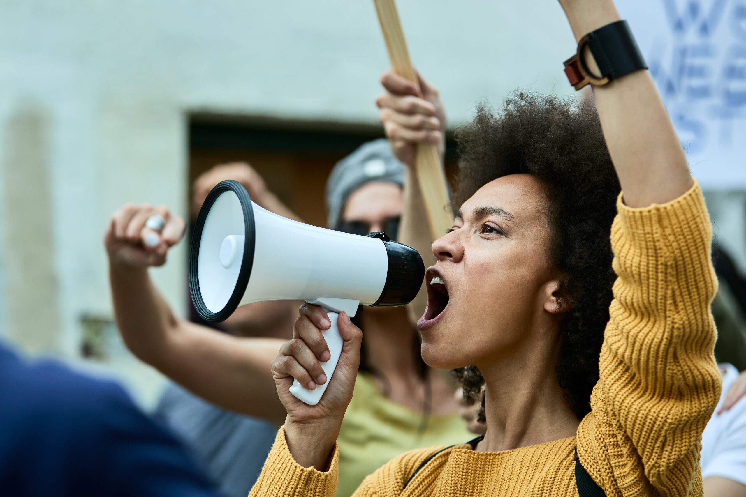 african american woman with raised fist shouting through megaphone on anti racism protest.