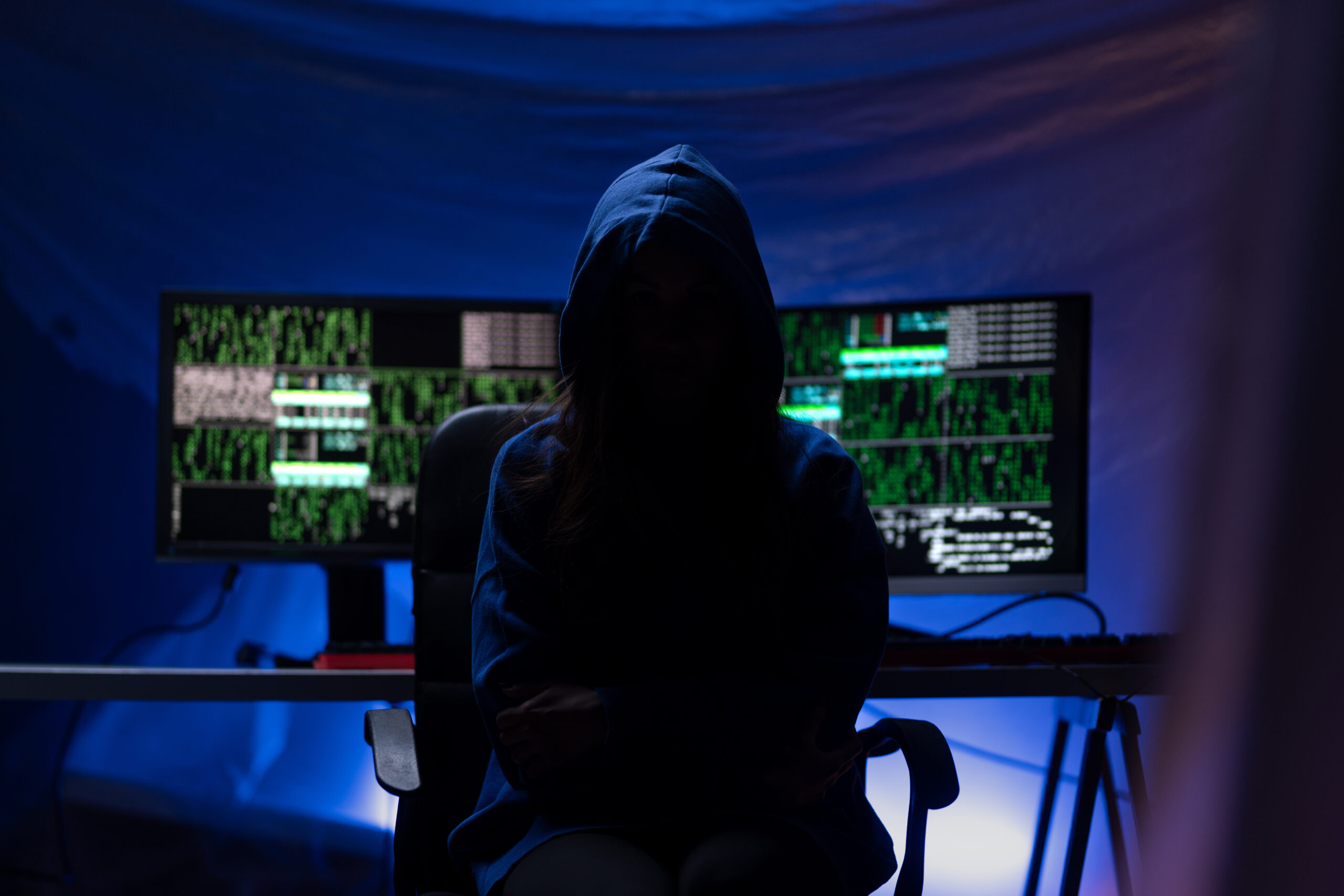 hooded anonymous hacker by computer in the dark room at night, cyberwar concept.