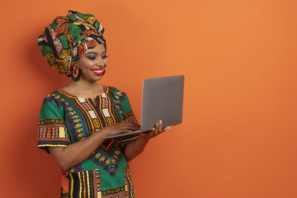 cheerful young black woman typing on laptop keyboard, orange background