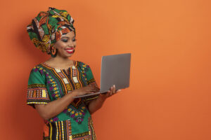 cheerful young black woman typing on laptop keyboard, orange background
