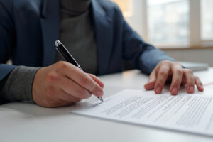 man signing contract in office with male hand holding pen