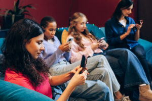 group of multinational young women sitting on couch using smartphones