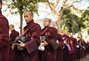 monks in maroon robes lining up for alms in serene morning light