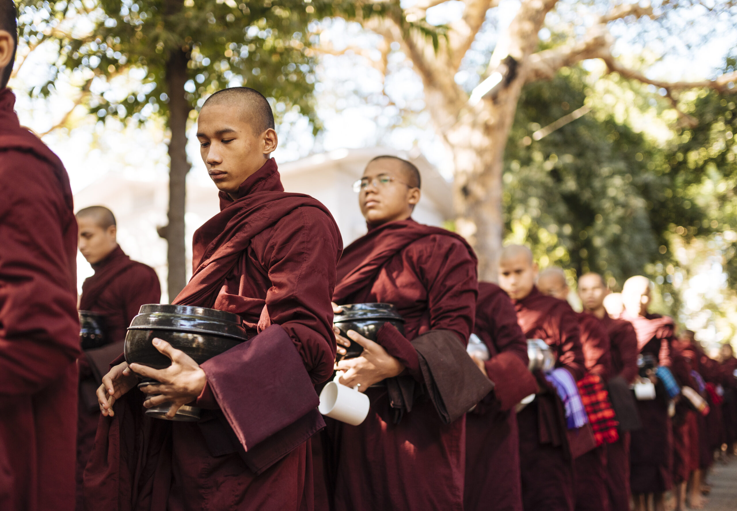 monks in maroon robes lining up for alms in serene morning light